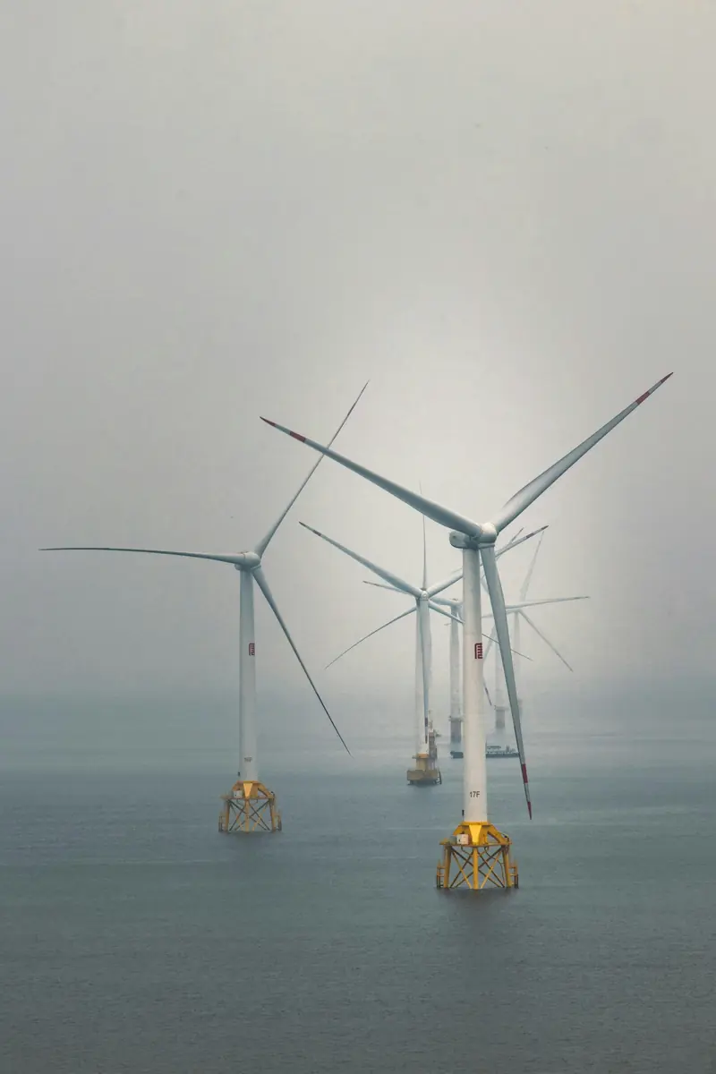 Offshore wind turbines standing in fog over a calm sea