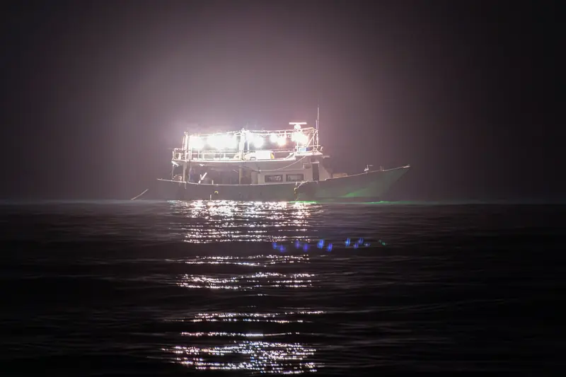 A fishing boat with its lamps lit at sea at night